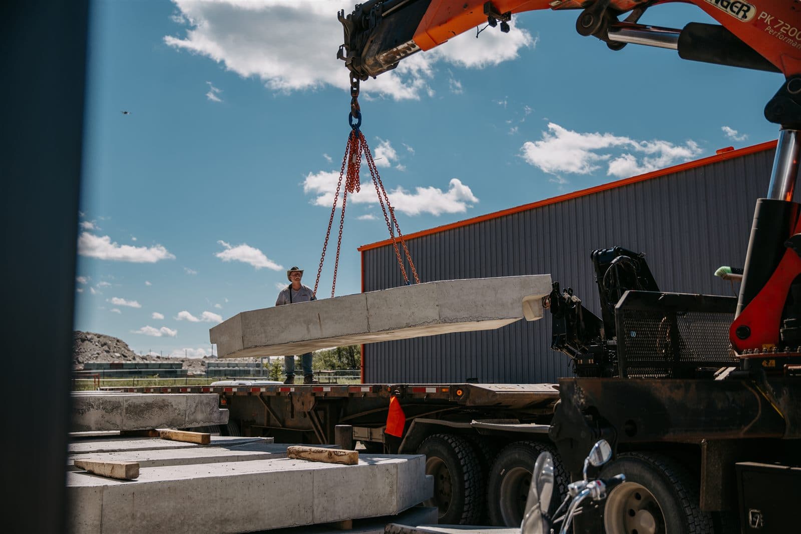 An AltaMix worker guiding a precast panel suspended from the crane truck over a flat-deck trailer.